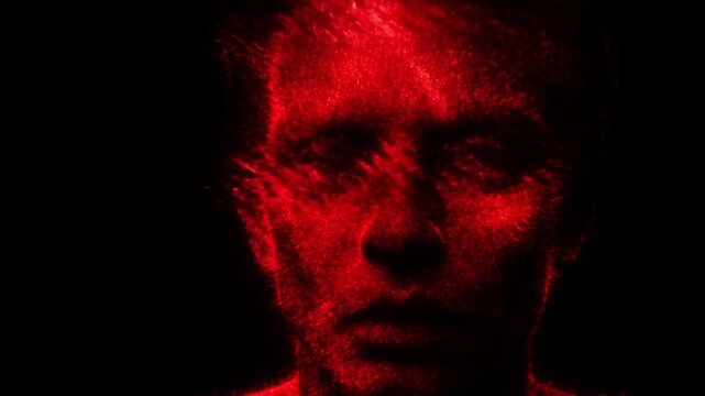 Slow motion closeup portrait of human face dissolving into red particles and dispersing across textured black studio background, static view