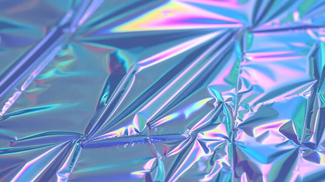 Slow pan shot of iridescent holographic foil shimmering and reflecting light on crinkled metallic sheet in studio close up