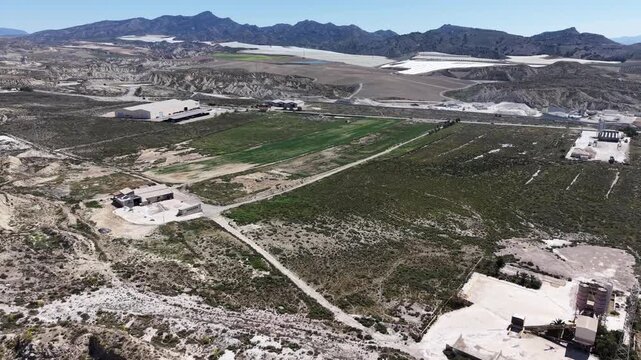 A tracking drone shot flying over an asphalt business and a factory with solar panels on the roof amidst a vast arid desert area.