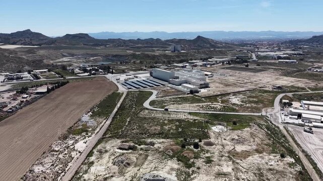 A tracking drone shot of an industrial factory with rooftop solar panels, surrounded by the arid badlands and mountains of the Lorca region in Murcia.