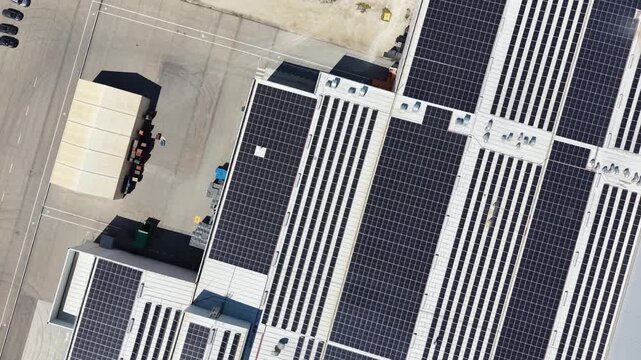 A top down drone shot moving over a large industrial warehouse roof covered entirely in solar panels, highlighting sustainable energy solutions in Murcia.