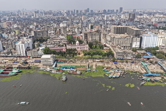 Dhaka, Bangladesh - 11 April 2026: Aerial view of the vibrant Buriganga River, choked with boats and green hyacinth, meeting Dhaka's dense, sprawling cityscape and the iconic pink Ahsan Manzil.