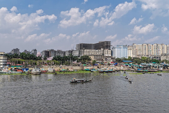 Dhaka, Bangladesh - 11 April 2026: Aerial view of the Buriganga River, its dark waters bearing boats against a vibrant, densely packed city skyline under a wide sky.