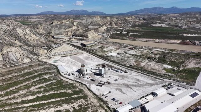 A back tracking drone shot of a cement and gravel factory near Lorca, showing the heavy machinery, silos, and raw materials under a bright sun in Murcia.