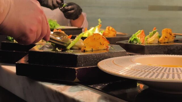 Professional chef uses tongs to plate traditional Vietnamese Bun Cha with snails in a modern Hanoi Old Quarter restaurant kitchen. Fine dining food preparation.