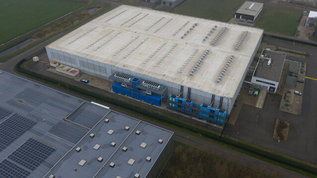 Roosendaal, Netherlands - 27 December 2025: Aerial view of the vast, angular datacenter, its pale roof contrasting sharply with the deep blue modules and verdant borders.