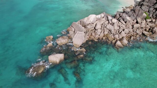 Panning drone of granite stones between grand anse beach and petite anse, along water, La Digue, Seychelles 30fps 006