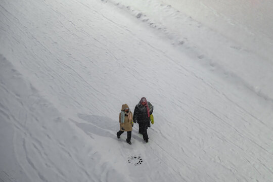 Tallinn, Estonia - 03 January 2025: View of two bundled figures trudging across a vast, pristine expanse of textured white snow, their dark forms a striking contrast against the pale winter landscape.