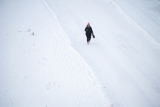 Tallinn, Estonia - 03 January 2025: View of a lone figure traversing a vast, rippled expanse of pristine white snow, a stark contrast to the dark attire and vibrant pink accents.