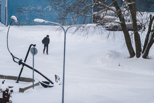Tallinn, Estonia - 03 January 2025: View of a stark winter scene with a lone figure walking across fresh snow, framed by dark streetlights and an imposing anchor structure.