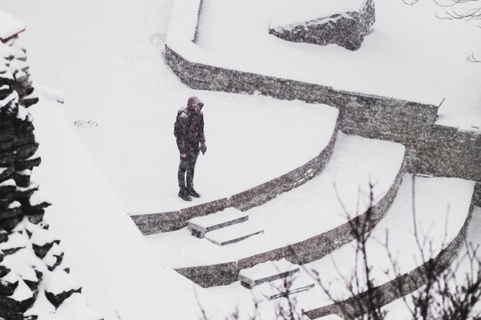 Tallinn, Estonia - 03 January 2025: View of a lone figure in dark attire stands on snow-covered grey stone terraces, a stark contrast against the pristine white winter.