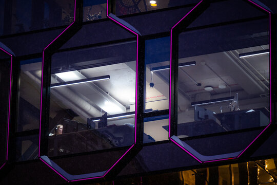 Tallinn, Estonia - 03 January 2025: View of the geometric honeycomb of windows reflecting the interior's stark fluorescent lights, while a lone figure works late into the night.