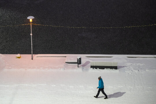 Tallinn, Estonia - 03 January 2025: View of a lone figure traversing a pristine, snow-covered path under the warm glow of a streetlamp, contrasting with the dark winter night.