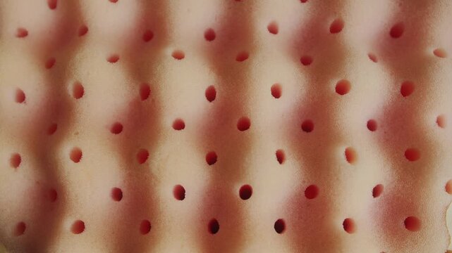 Close-up of perforated memory foam texture with soft rounded shapes and breathable structure. Abstract background representing comfort, support, and modern material design. High quality 4k footage
