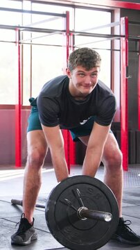 Vertical video: Finishing set, trainee in dark tee lowering landmine bar, hugging red shirt trainer