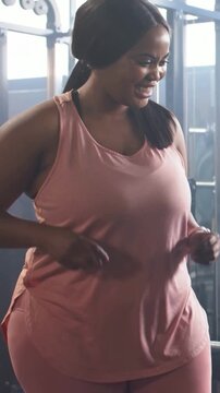 Vertical video: Warming up woman in pink outfit stepping in gym checking smartwatch by weight rack