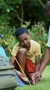Vertical video: Adult positioning stake while kid in yellow hammering mallet securing tent on grass
