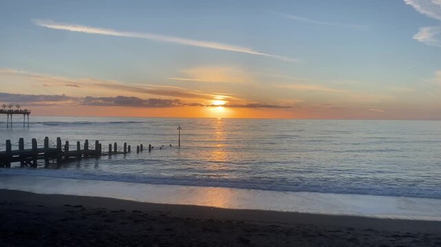 Stunning 4K landscape footage of a peaceful, semi-calm sea at Aberystwyth, Wales, featuring a small wooden jetty or breakwater extending into the water.