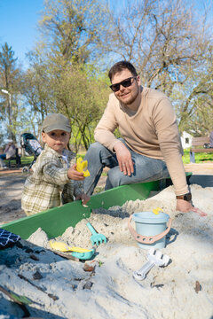 Father and son playing in sandbox outdoors on sunny day.