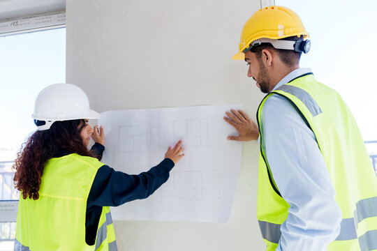 Architect explaining blueprint to colleague at site