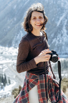 Smiling photographer with camera in snowy mountain landscape