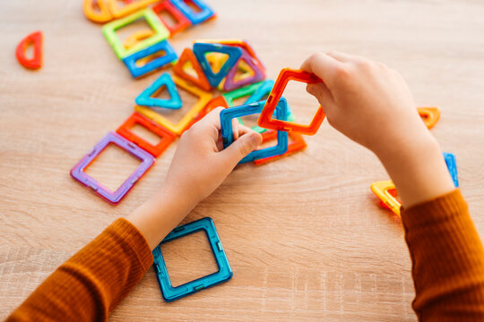 Child hands playing with magnetic construction toy on wooden table