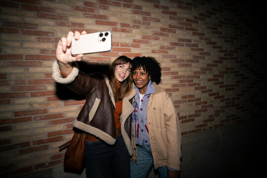 Friends taking a smiling selfie with a smartphone at night