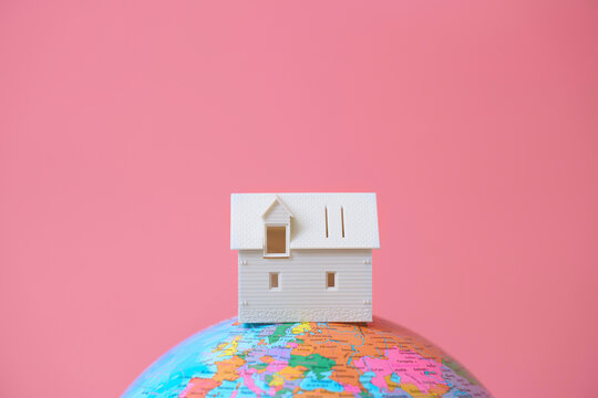 White model house on a globe against a pink background