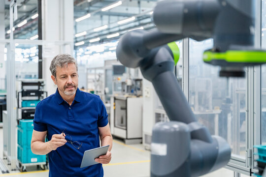 Employee with tablet in automated factory with industrial robot portrait