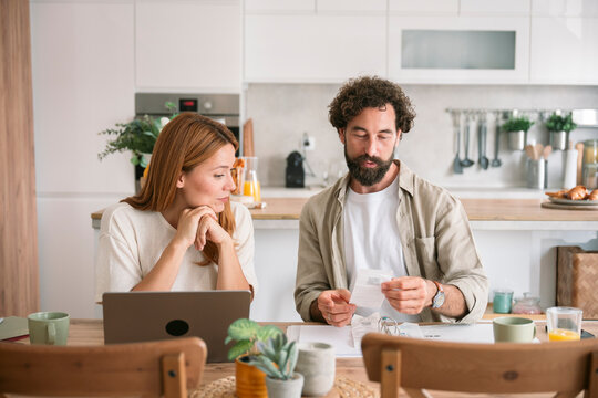 Couple checking invoices and using laptop at kitchen table