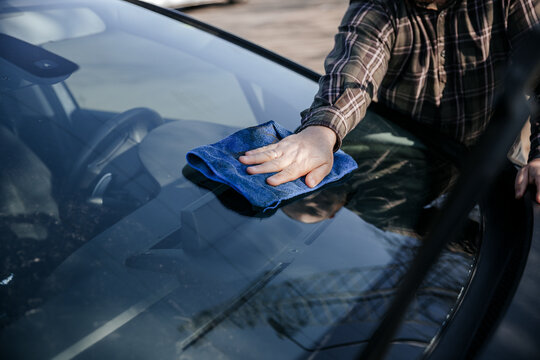 Hand cleaning car windshield with microfiber cloth outdoors