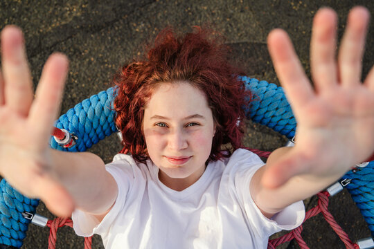 Cheerful girl reaching out while swinging at the outdoor playground