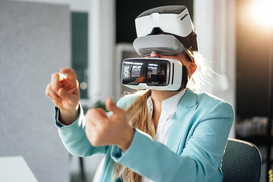 Mature businesswoman wearing virtual reality headsets gesturing at office