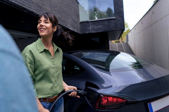 Happy businesswoman charging electric car in parking