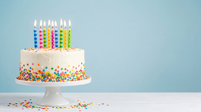 Colorful birthday cake with lit candles and sprinkles on blue background