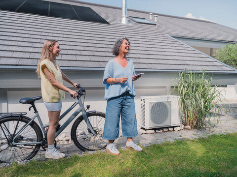 Mother and daughter with bike smiling near house with solar panel