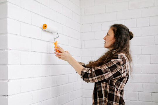 Homeowner in plaid shirt painting white brick wall indoors