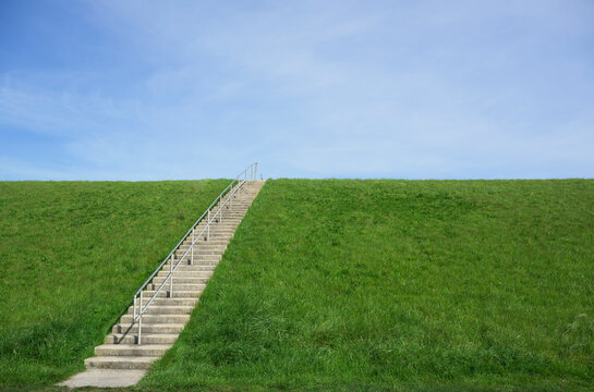 Concrete staircase on a green grassy dyke against a blue sky