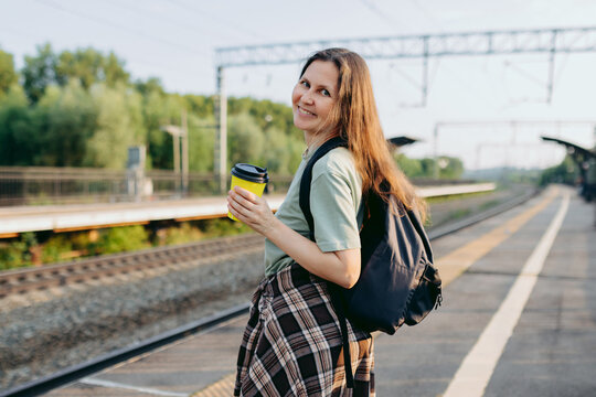 Commuter with backpack and coffee waiting on railway platform