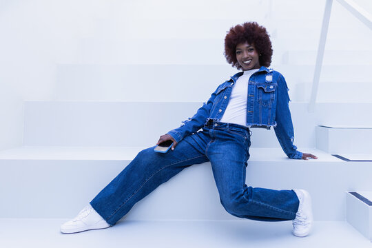 Smiling model in denim posing on a staircase with a smartphone