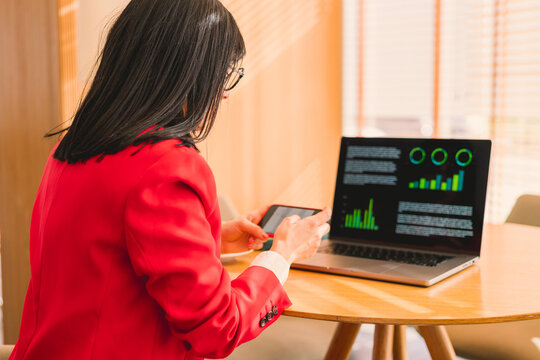 Businesswoman using smartphone and laptop for analytics indoors