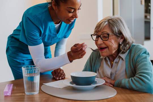 Healthcare worker feeding elderly woman at home enjoying meal