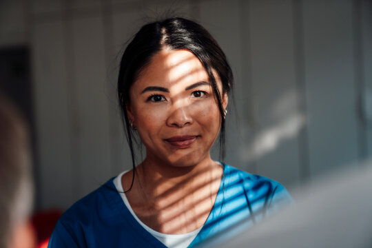 Nurse in blue uniform taking a break indoors with sunlight and shadows