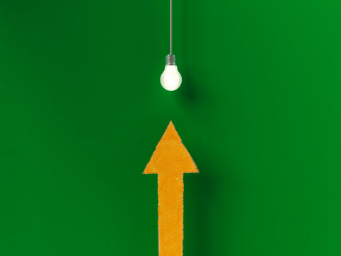 Upward pointing orange arrow and glowing lightbulb on green