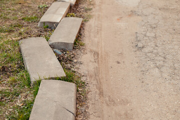 Fototapeta premium Concrete blocks line the edge of a dirt path while grass grows alongside. The scene depicts a simple outdoor setting that shows an interaction between natural and man-made elements
