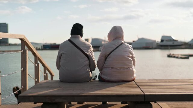 A man and a woman sit in warm clothes and shrivel at sea. The view from the back, without a face.