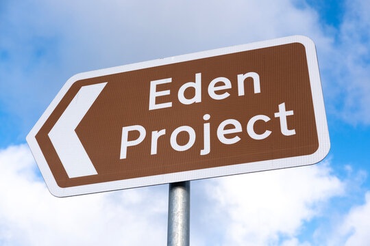 Low angle view of a brown information road sign, with directional arrow reading Eden Project, against a blue sky with white clouds.