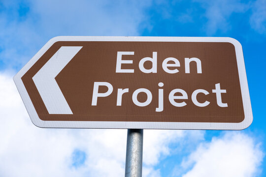 Low angle view of a brown information road sign, with directional arrow reading Eden Project, against a blue sky with white clouds.