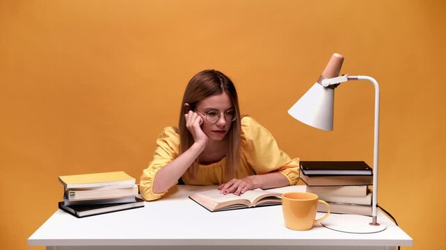 Tired female student falling asleep at her desk while studying with books for an upcoming exam late at night