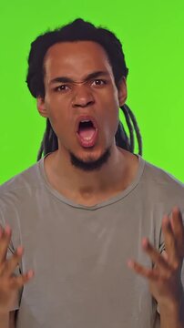 Angry young African American man with dreadlocks vents frustration, gesturing wildly and reacting with intensity against a green screen background, expressive emotion driven scenes